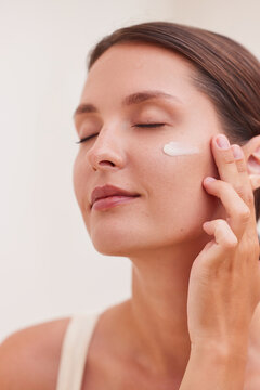 Face moisturizer woman with cream stripe on cheek looking up sideways, anti aging skincare routine, vertical close up portrait