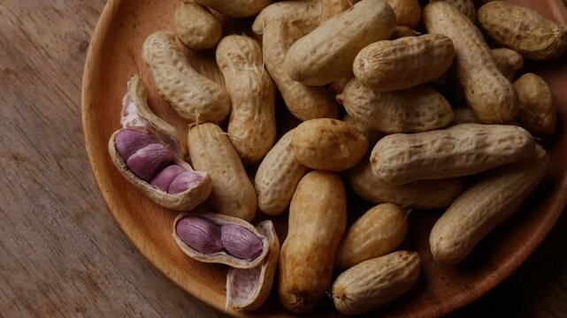 Boiled peanuts in shell with purple violet skin kernels revealed on wooden plate on rustic wood table, healthy traditional Asian snack nutrition closeup