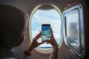Woman taking photo of airplane wing through window with smartphone © Ibenk.88