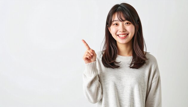 白い背景で左上を指しながら笑顔でカメラ目線の20代日本人女性