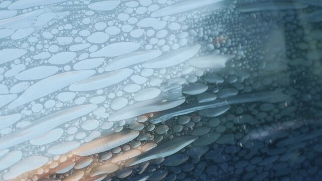 Air bubbles trapped in old deteriorated car window tint film, damaged adhesive layer on glass surface with peeling texture, vehicle maintenance problem and poor installation concept
