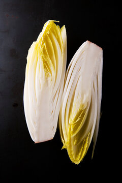 Vertical Hald-Sliced Fresh Belgian Endive Witloof White Chicory Vegetable on Black Background