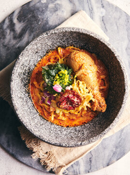 Top View of Khao Soi Gai Northern Thai Curry Egg Noodle with Chicken Drumstick Served in Stone Bowl