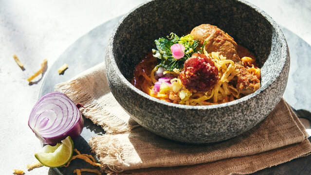 Close-up Khao Soi Gai Northern Thai Cuisine Dish Spicy Yellow Curry Egg Noodle with Chicken Drumstick Served in Stone Bowl