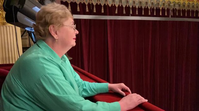 Senior happy woman is interested in watching ballet performance in theater hall, woman claps and enjoy