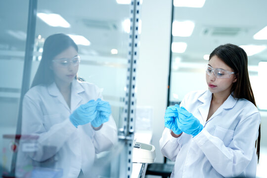 A microbiologist performs aseptic techniques in a laminar flow hood. She is processing a biological sample for pharmaceutical research and drug development.
