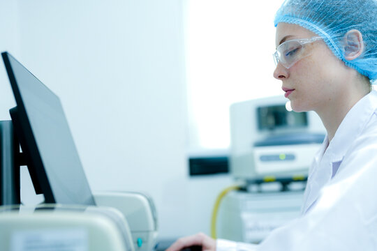A pathologist analyzes digital results on a computer screen. She is conducting pharmaceutical research or diagnostic testing in a sterile biotech lab, using automated systems.
