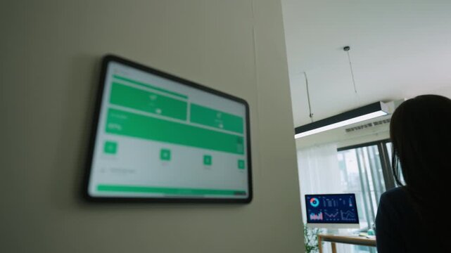 Modern woman adjusts smart lighting in her connected home office using a digital tablet, blending smart home tech, productivity, and comfort in a flexible, energy-efficient remote work environment
