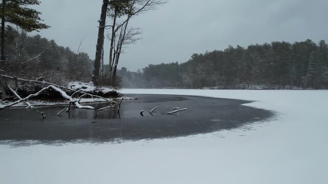 Low angle drone view of frozen lake, ice and snowy trees at Harold Parker State Forest, Massachusetts, USA
