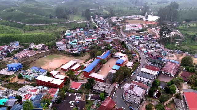 Wide cinematic aerial of Valparai highlighting compact urban layout, bright rooftops, central road activity, and surrounding plantation landscapes creating a lively mountain town atmosphere.