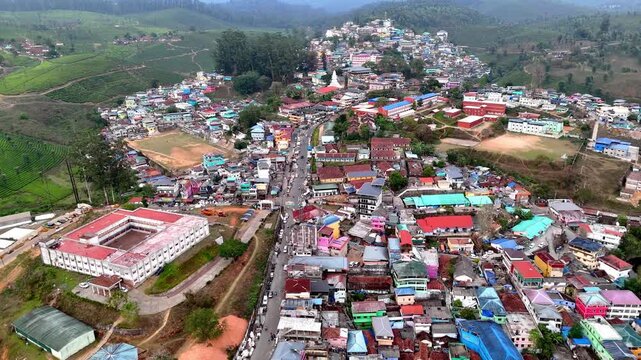 Cinematic aerial view of Valparai showcasing a vibrant hill town with colorful rooftops, dense housing clusters, winding roads, and surrounding tea plantations blending urban life with scenic greenery