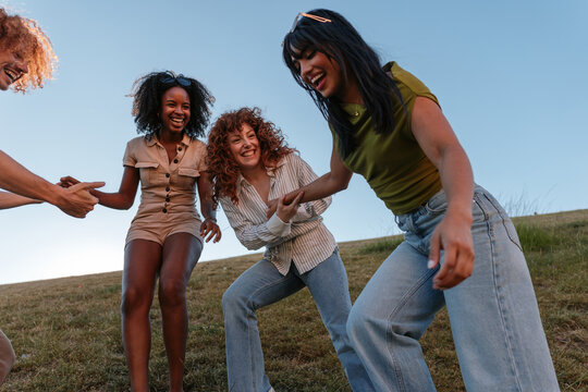 Diverse friends laughing and holding hands on hillside