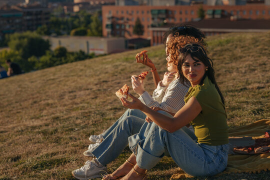Diverse girlfriends enjoying pizza picnic at sunset