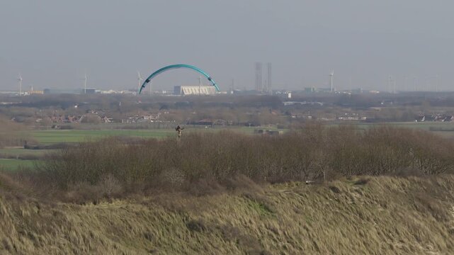 Drone orbits paraglider flying over Zoutelande coastal landscape with wind turbines