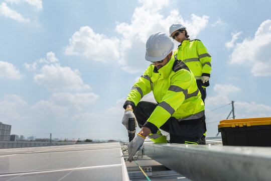 Professional technicians using electric drill to mount photovoltaic panels for renewable energy, Maintenance workers in safety gear installing sustainable solar energy systems on a commercial building