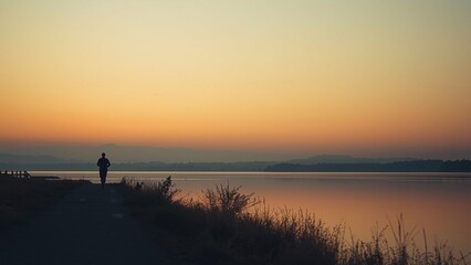 Fototapeta premium Distant jogging silhouette by a lakeside path, minimal scene, soft cloudless sunset sky with warm gradient, subtle layers of path, water, and sky, calm cinematic, clean and simple aesthetic.