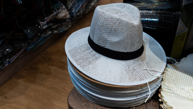 a neatly stacked pile of new white woven fedora hats with a black fabric ribbon band on a retail display counter in a souvenir shop for summer vacation