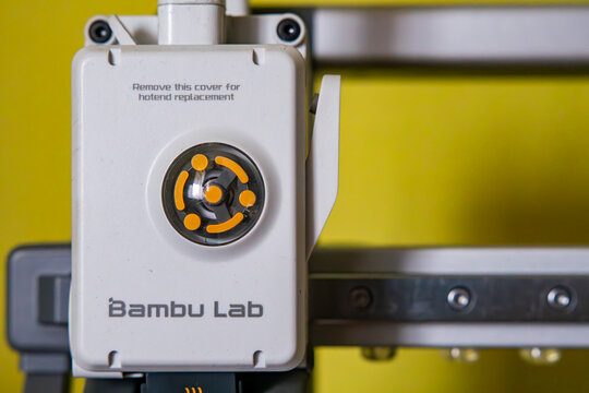 Close-up of Bambu Lab 3D printer print head, modern extruder and hotend assembly for additive manufacturing, advanced prototyping technology and digital production, technical detail on yellow backgrou