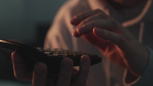 Close-up of a financial analyst or accountant calculating numbers on a calculator in a dark room. Focus on hands performing financial calculations, budgeting, and business analysis. Concept of economi