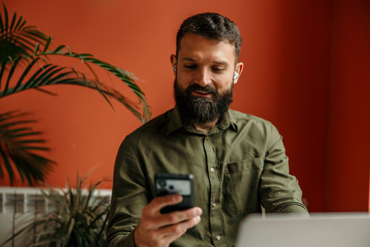 Man with beard using smartphone and earbuds