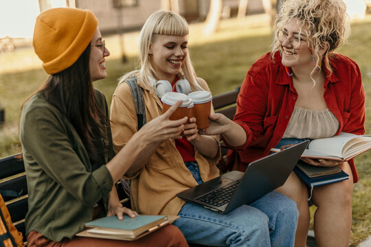 Happy students toasting coffee on campus bench