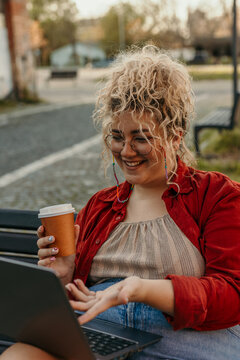Woman working remotely laughing outdoors with coffee