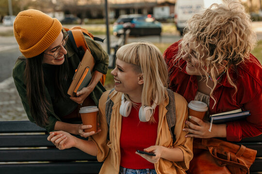 Happy college friends laughing enjoying coffee outdoors