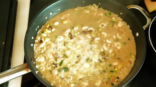 Rice, courgettes and shrimp cook in a pan to make a risotto. The video was shot in the kitchen of an apartment while preparing a risotto with courgettes and shrimp
