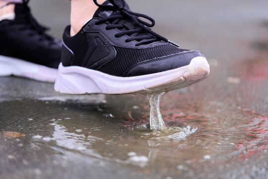 Person walks in rain and splashes water with shoes on wet pavement during a cloudy day
