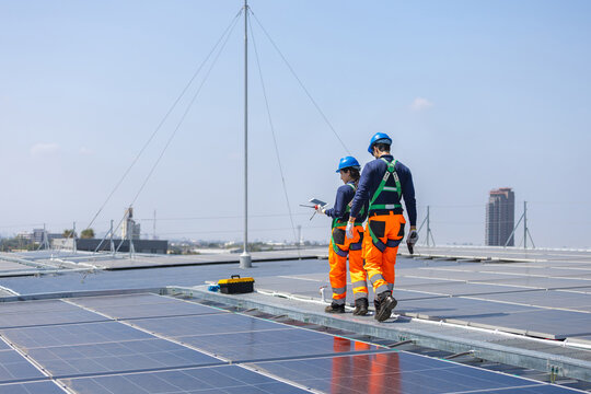 Engineers in safety uniform walking on solar rooftop, Professional technical team discussing maintenance of solar panel system, Workers inspecting renewable energy station on building roof
