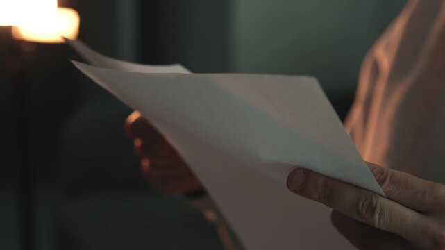 Close-up of a person reading important documents or notes on white paper in a dimly lit room. Concept of journalism, investigation, information review, and document analysis. Focused attention