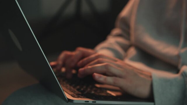 Young freelancer working on laptop at home, typing and coding in the evening. Remote work, IT profession, software development, online job, and productivity concept. Scene of focused work