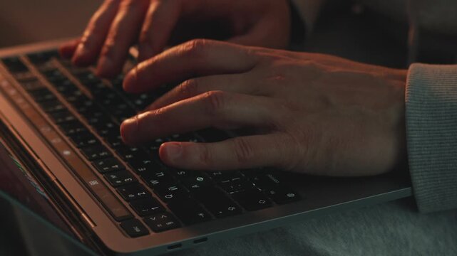 Young freelancer working on a laptop in his room in the evening. He types on the keyboard, focused on remote IT work and programming tasks. Concept of home office, digital profession, and productivity