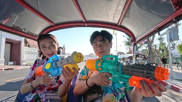 Asian Couple Celebrating Songkran Festival with Water Guns in a Tuk Tuk