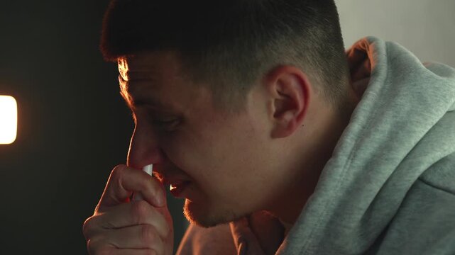 Person using nasal spray in a dark room to relieve nasal congestion. Concept of cold, allergy symptoms, breathing problems, and home treatment. Close-up, low light, healthcare and self-care routine.