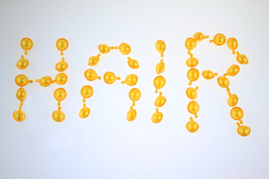 Golden beads spell "HAIR" against a clean white background. Each bead links to form the word with soft, glowing texture.  For self care, hair treatment, beauty concept, and modern cosmetic design.  