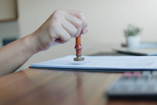 Notary public hand using wooden rubber stamp legal contract paper desk official document authorization corporate partnership agreement validation law firm administration concept.