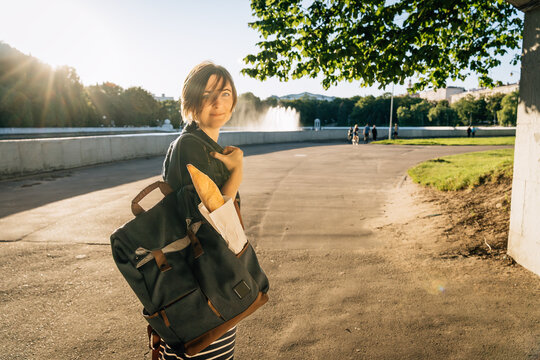 Smiling woman 40 with backpack carrying baguette in park