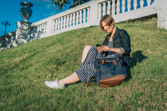 Woman in striped dress sitting on grass slope using smartphone