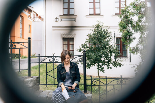 Mature woman checking phone on stone stairs blurred railing foreground