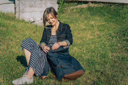 Woman reaching into backpack while sitting on grass in park