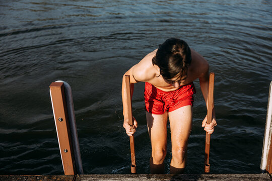 Teenager climbing up dock ladder from lake swim