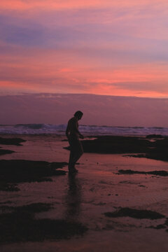 Man walking barefoot through tide pools at pink and purple sunset