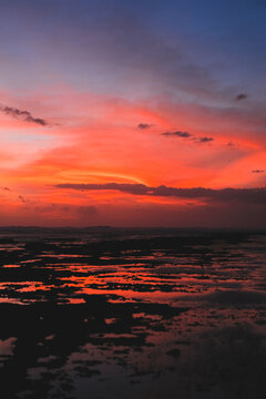 Vivid fiery orange and red sunset over rocky tidal flats and ocean