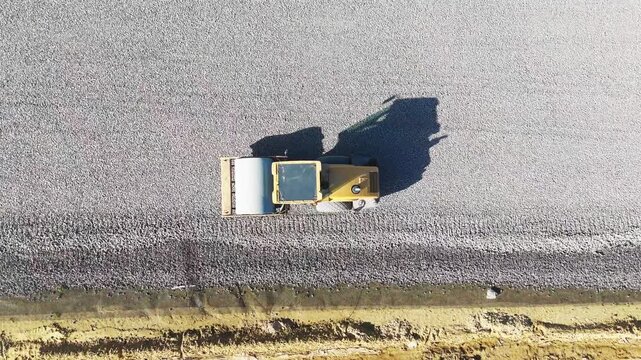 A heavy roller is rammed into the gravel foundations during the construction of a new road. View from above. Road construction machinery. High quality 4k footage