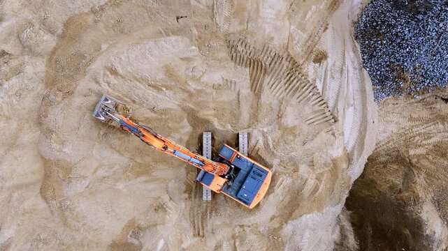 An excavator is engaged in moving soil in a sand quarry top view from a quadcopter. Excavation with the help of heavy construction machinery in quarries, mining and extraction of kh minerals. High