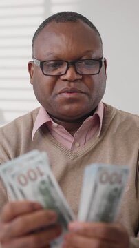 Senior african american male person counting cash, closeup view of hundred dollars banknotes and blurred male face, economy and salary, stingy and greedy man, dream about richness and wealth, portrait