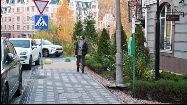 Young Man Walking on a European Cobblestone Street with Coffee Cup in Autumn Cityscape