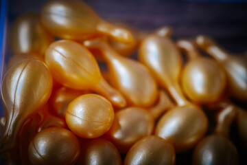 Macro image of several gold serum capsules scattered on a surface, showcasing a shiny texture, even shape, and rich cosmetic appeal with a soft background blur. © Jolanta