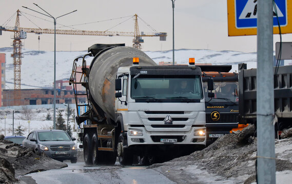 Kazakhstan, Ust-kamenogorsk, march 9, 2026: Traffic. City street. Concrete mixer and dump trucks. Tower cranes. Buildings under construction. Ped xing. Grunge urban cityscape